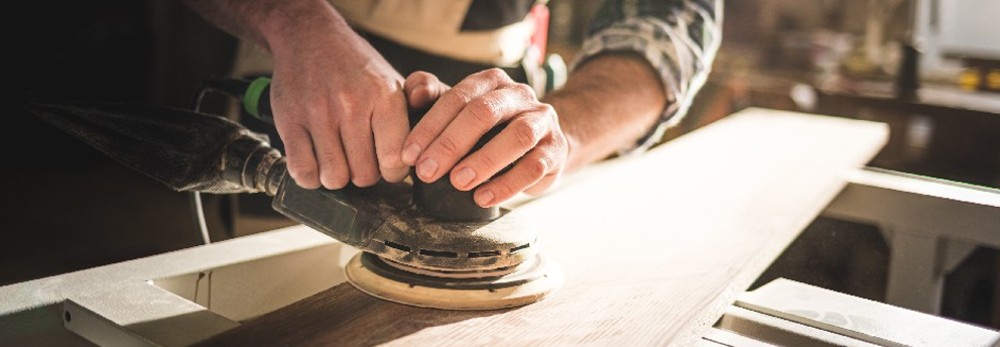 Person schleift Holzbrett mit Schleifmaschine